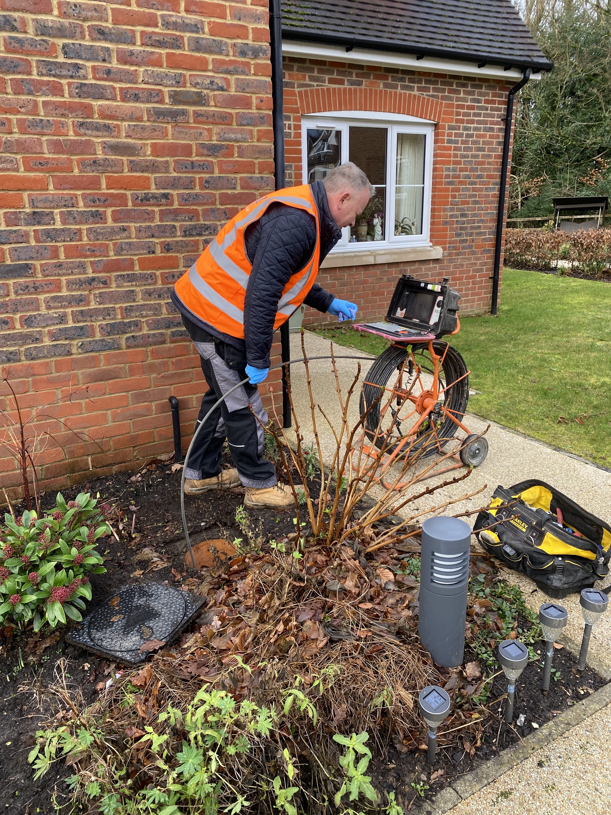 G-Force engineer running a CCTV drain camera at a manhole in a front garden